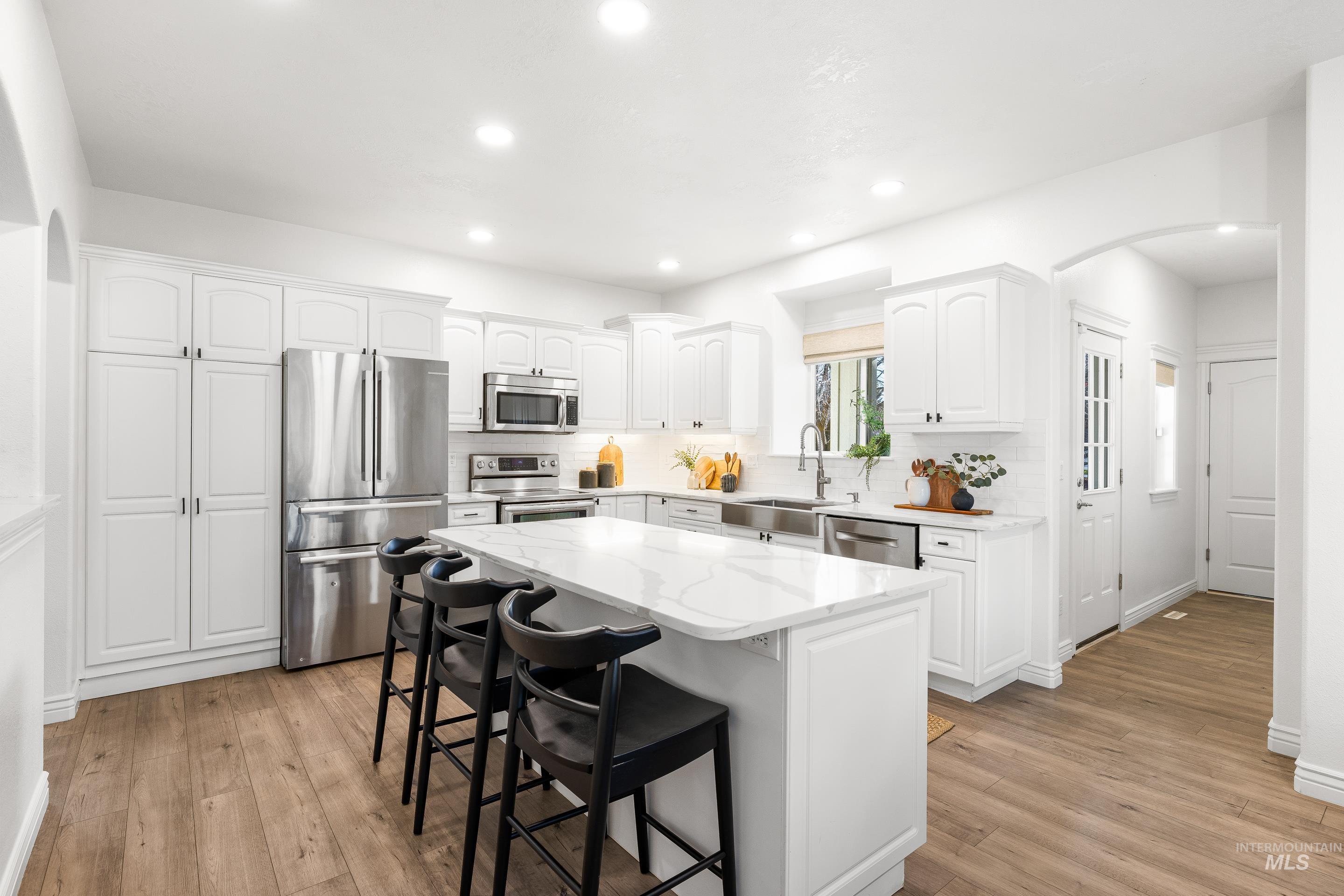 Kitchen featuring stainless steel appliances, white cabinetry, light wood finished floors, a breakfast bar area, and arched walkways
