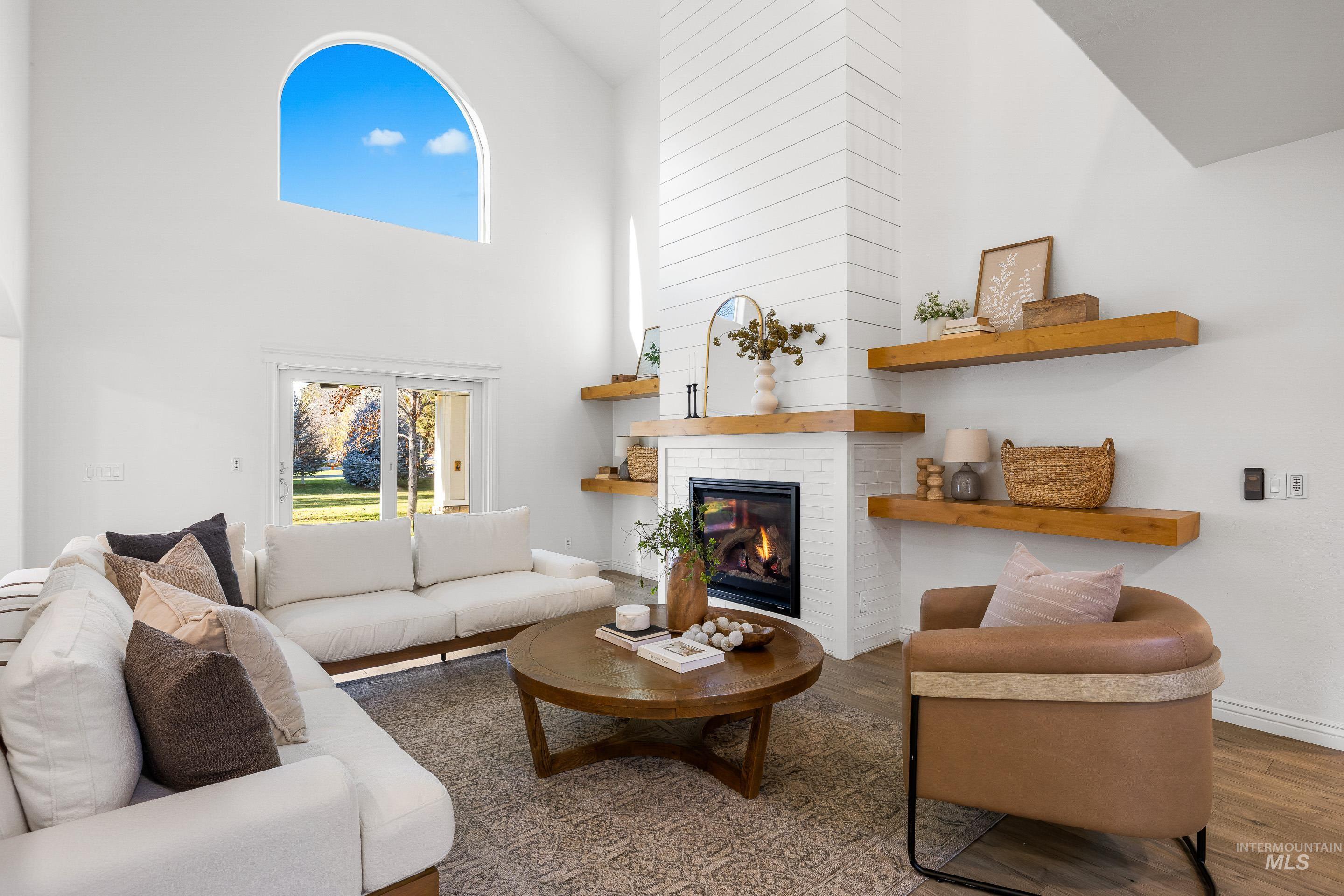 Living area with high vaulted ceiling, a brick fireplace, wood finished floors, and healthy amount of natural light