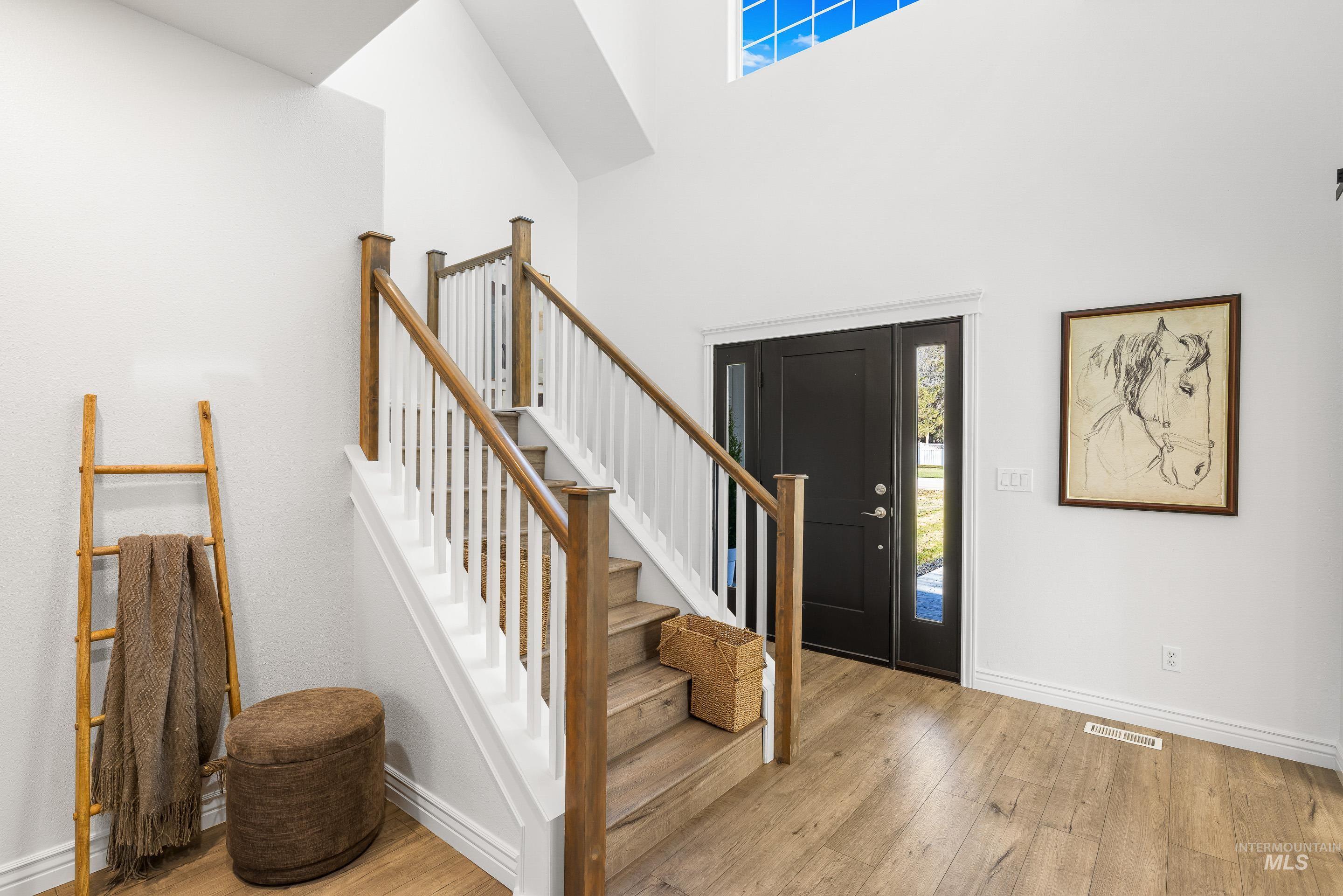 Entryway featuring stairway, light wood-style flooring, and a towering ceiling
