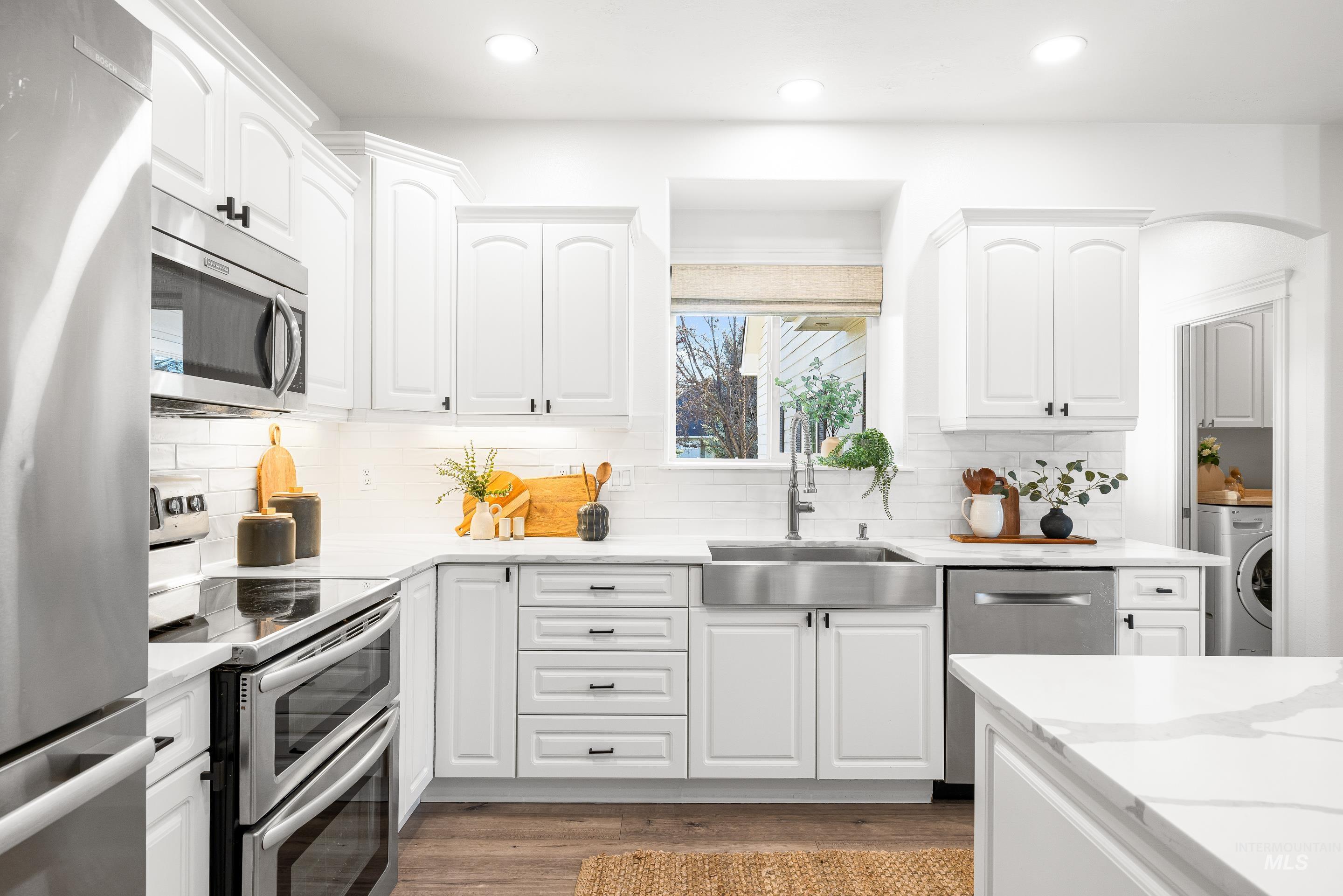 Kitchen with appliances with stainless steel finishes, white cabinets, light stone counters, light wood-style floors, and recessed lighting