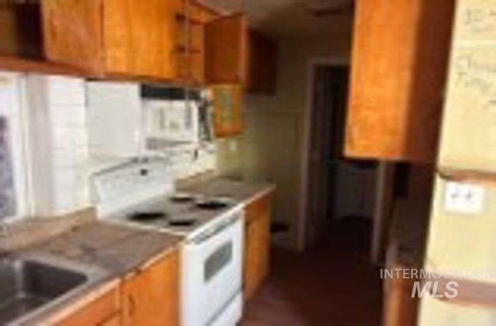 Kitchen with white appliances, brown cabinetry, and light countertops