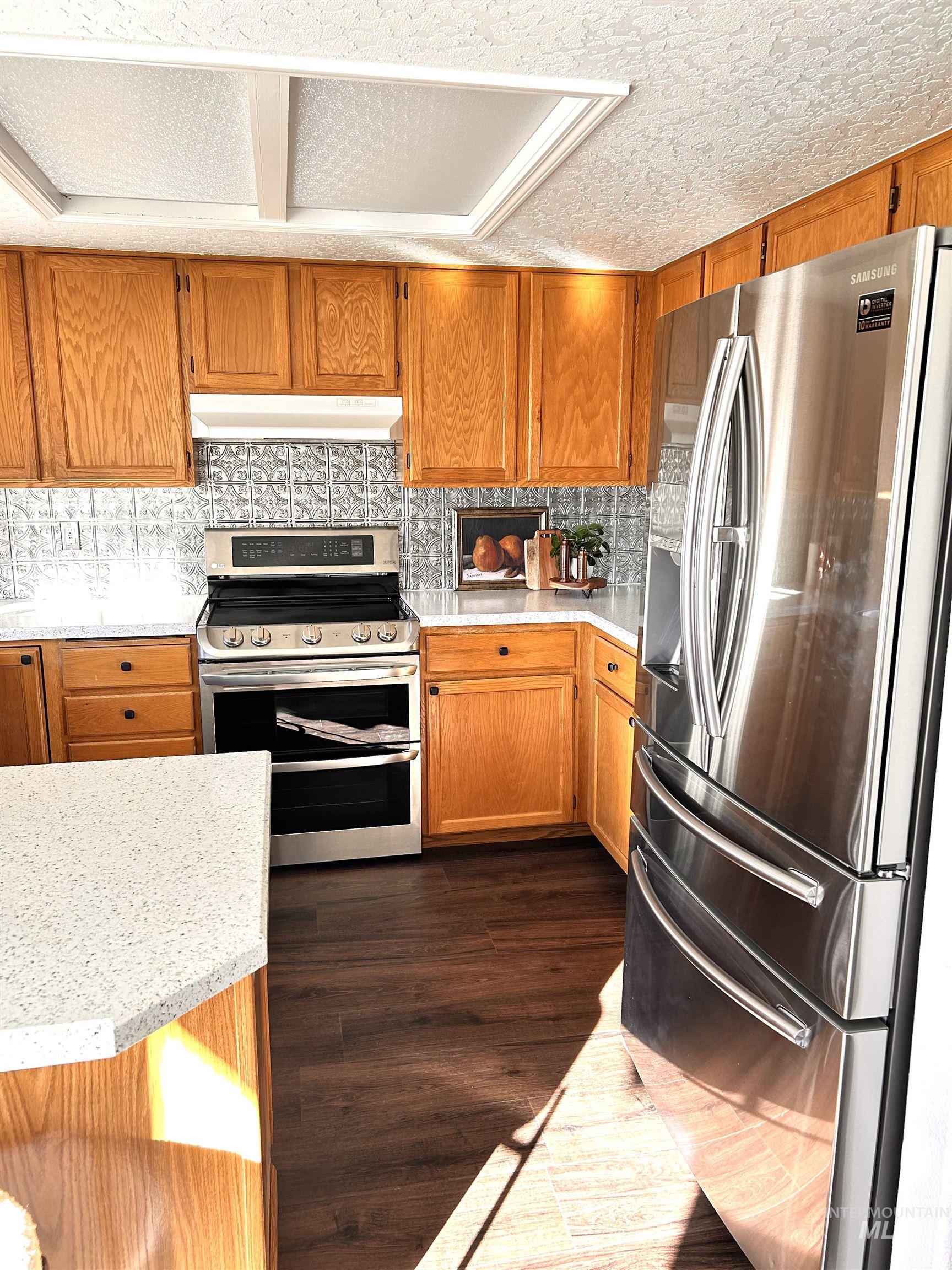 Kitchen featuring stainless steel appliances, brown cabinetry, decorative backsplash, and a textured ceiling