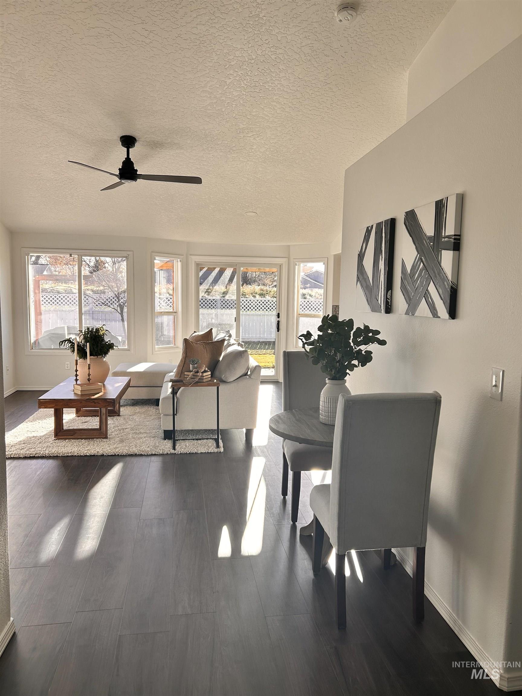 Living area featuring healthy amount of natural light, a textured ceiling, dark wood-style flooring, and a ceiling fan