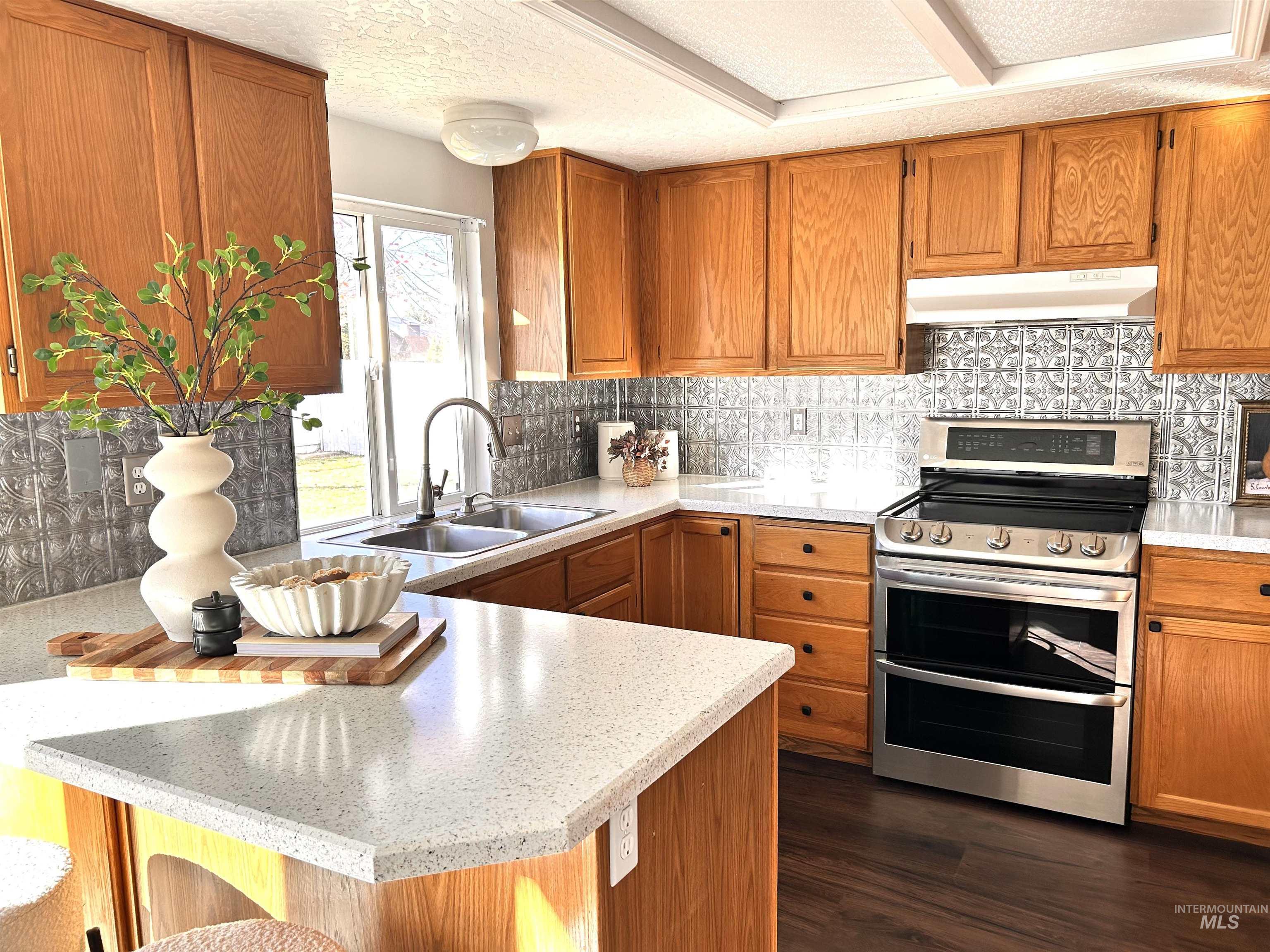 Kitchen with range with two ovens, brown cabinetry, a peninsula, a textured ceiling, and under cabinet range hood