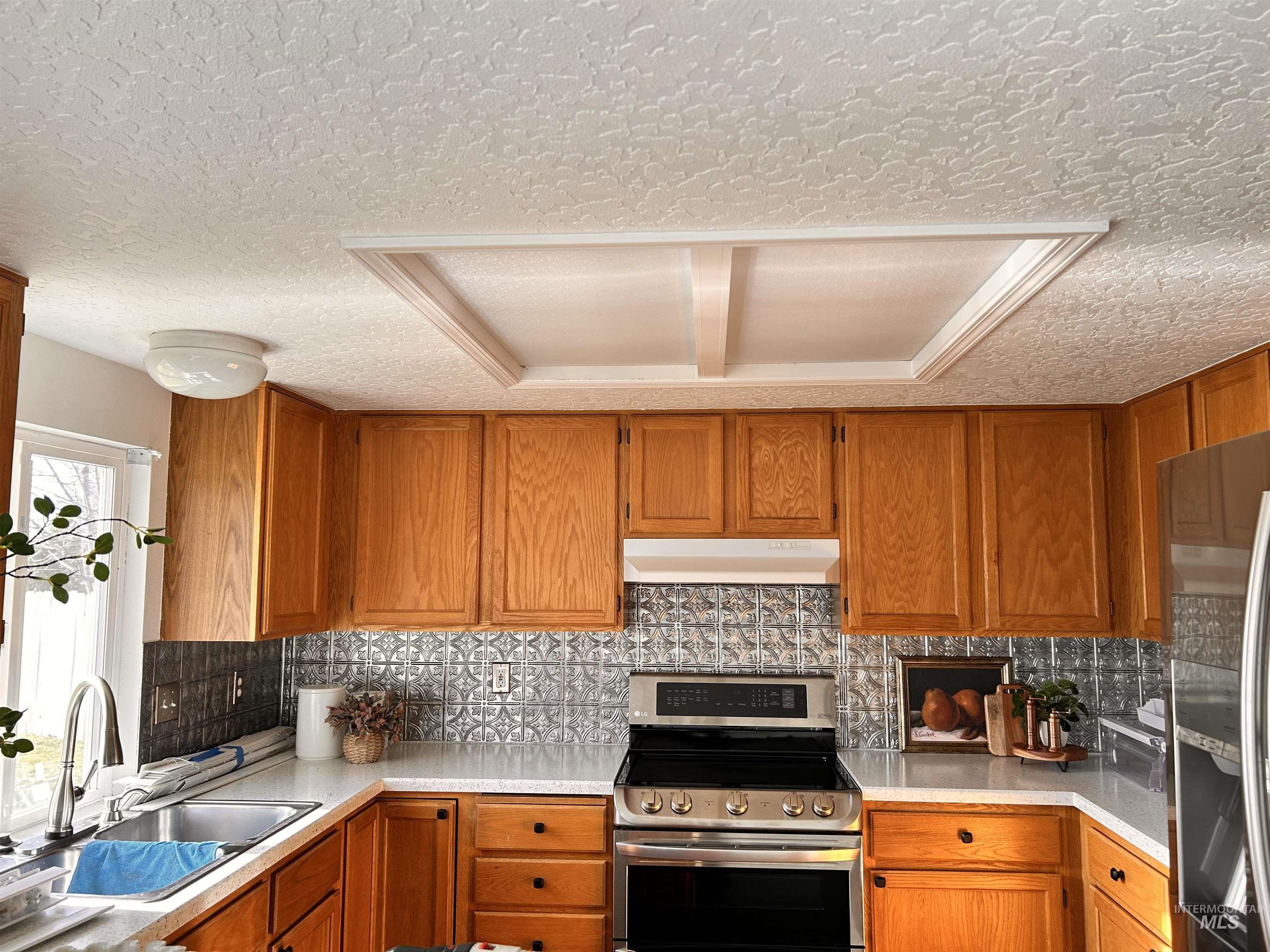 Kitchen with appliances with stainless steel finishes, brown cabinets, tasteful backsplash, under cabinet range hood, and a textured ceiling