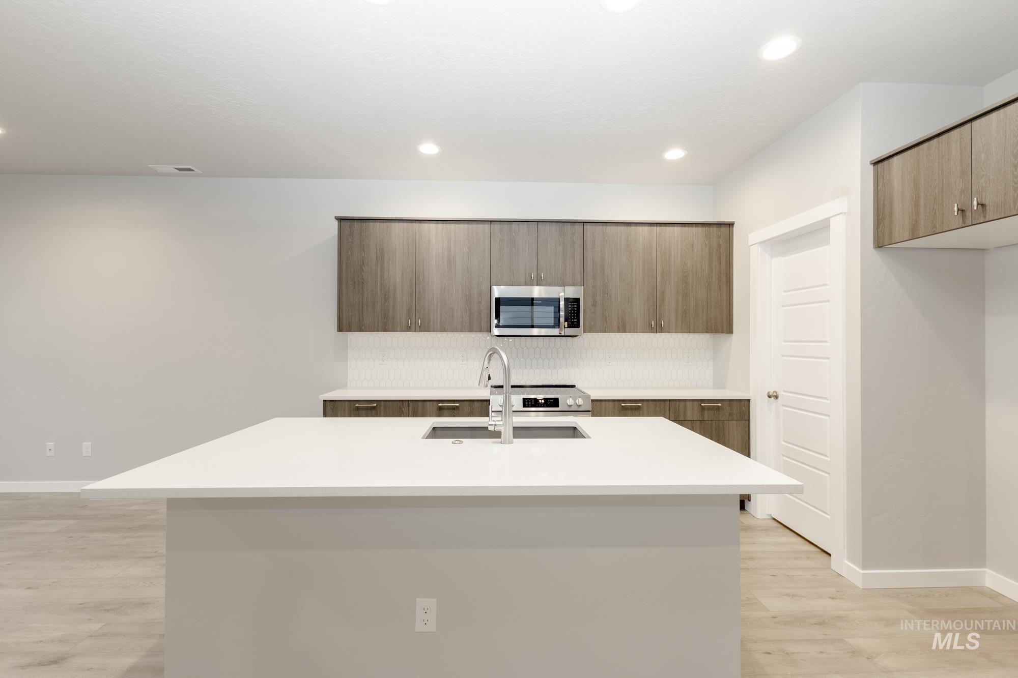 Kitchen with stainless steel appliances, a center island with sink, modern cabinets, light wood-type flooring, and brown cabinetry