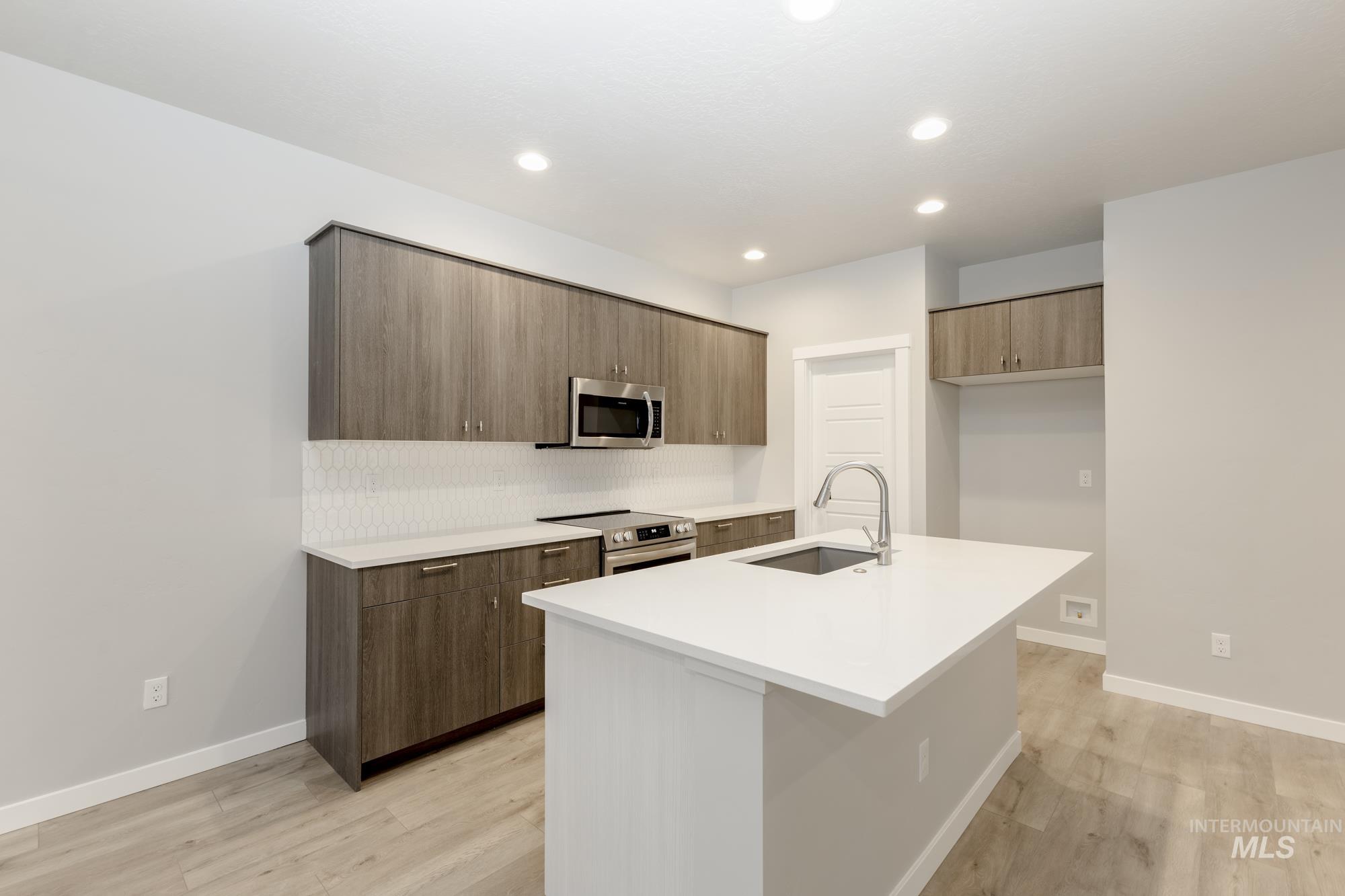 Kitchen featuring modern cabinets, stainless steel appliances, tasteful backsplash, a kitchen island with sink, and light wood finished floors