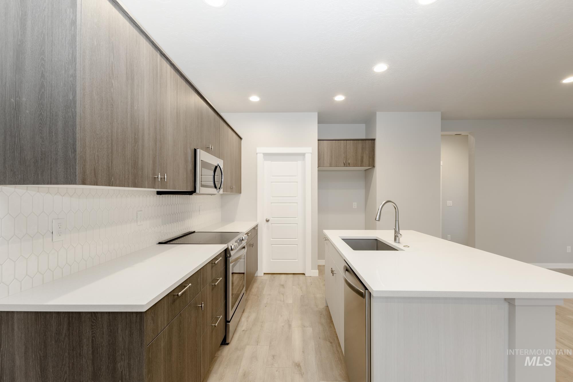 Kitchen featuring modern cabinets, appliances with stainless steel finishes, light wood-style flooring, decorative backsplash, and an island with sink