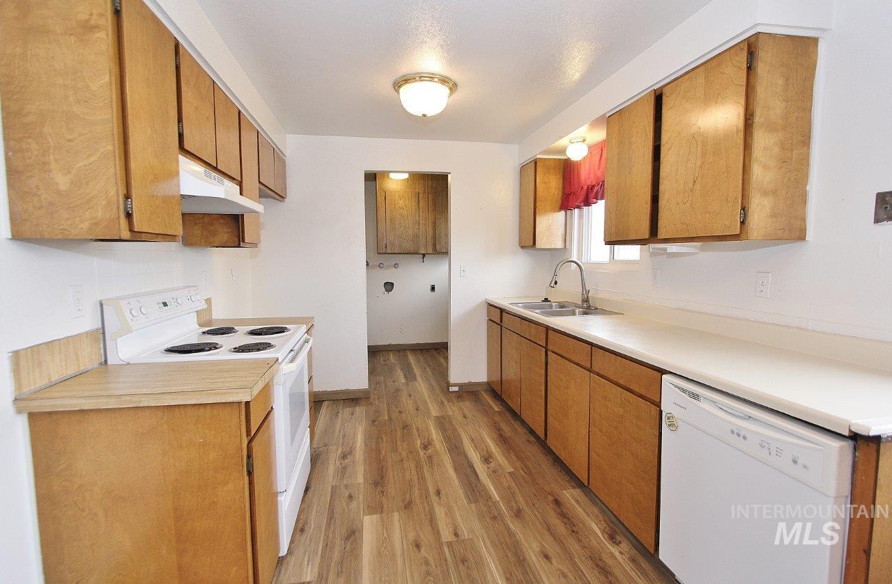 Kitchen featuring white appliances, under cabinet range hood, light wood-type flooring, light countertops, and brown cabinets