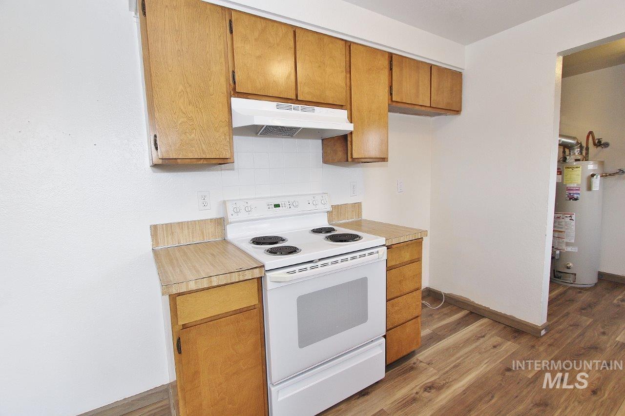 Kitchen with white electric range oven, light countertops, under cabinet range hood, light wood finished floors, and gas water heater