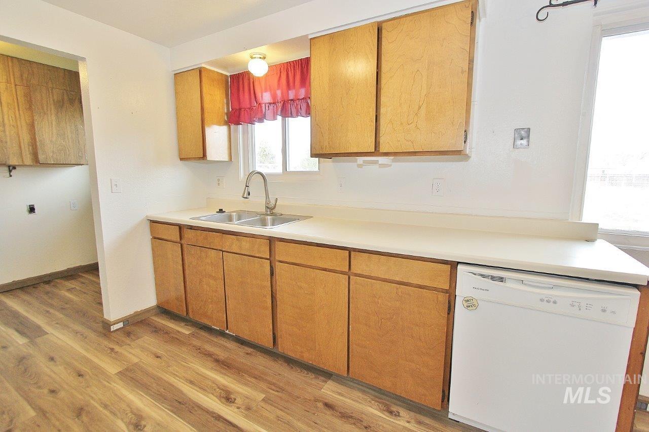 Kitchen featuring white dishwasher, light countertops, brown cabinets, and light wood-type flooring