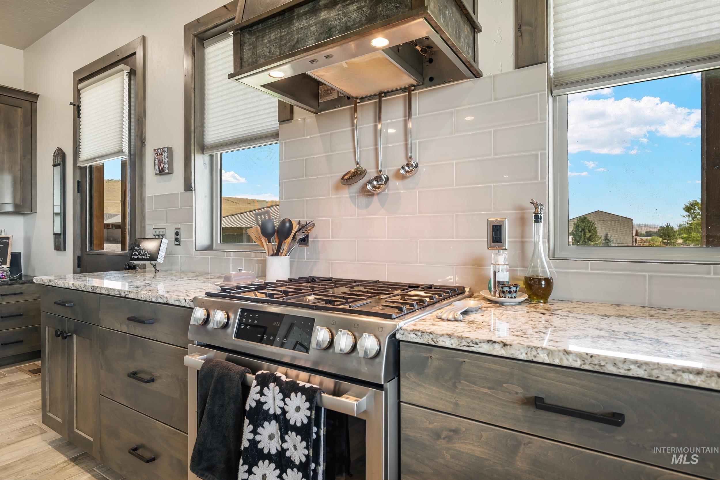 Kitchen with stainless steel range with gas stovetop, exhaust hood, tasteful backsplash, and light stone countertops
