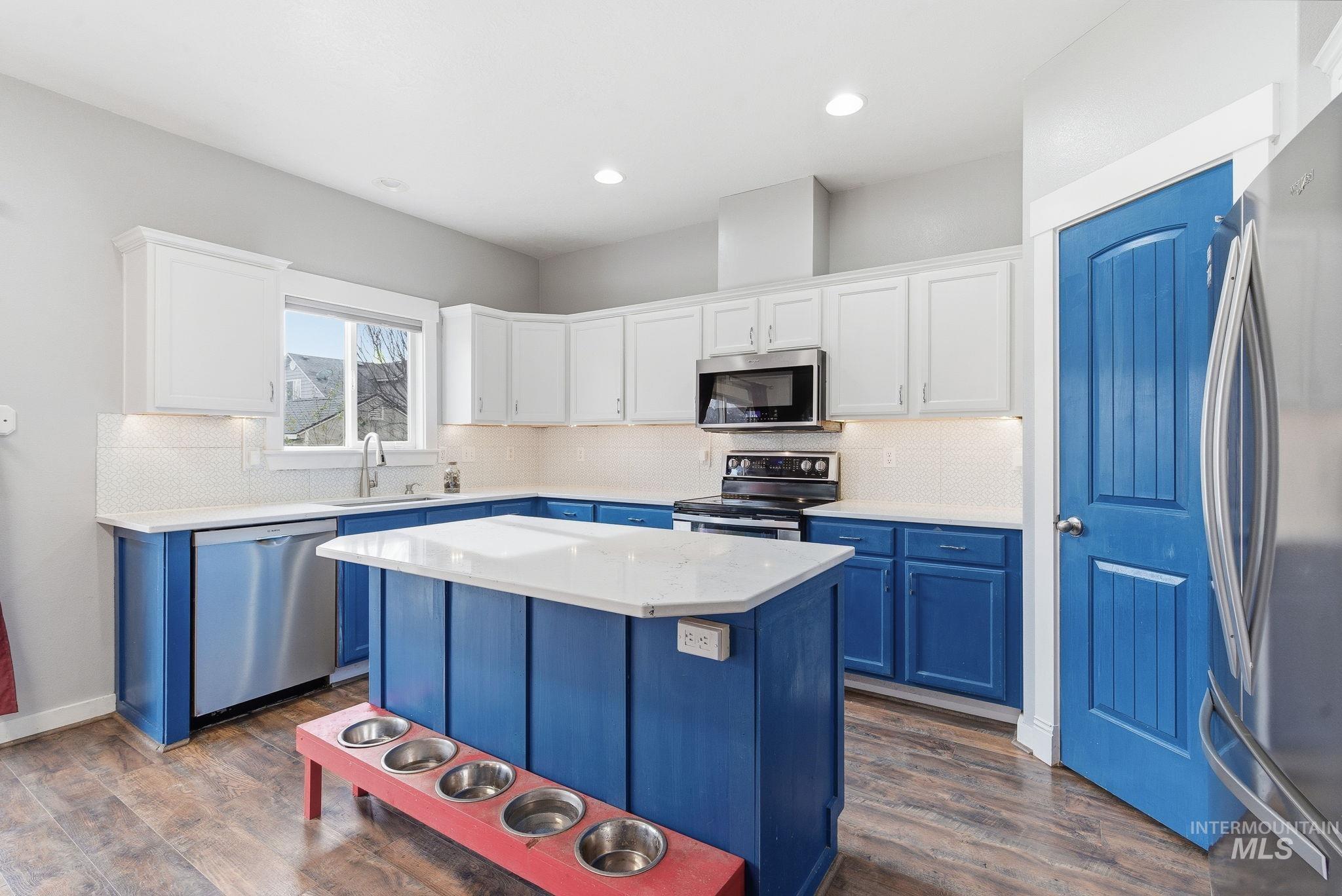 Kitchen featuring blue cabinetry, stainless steel appliances, white cabinets, a center island, and tasteful backsplash