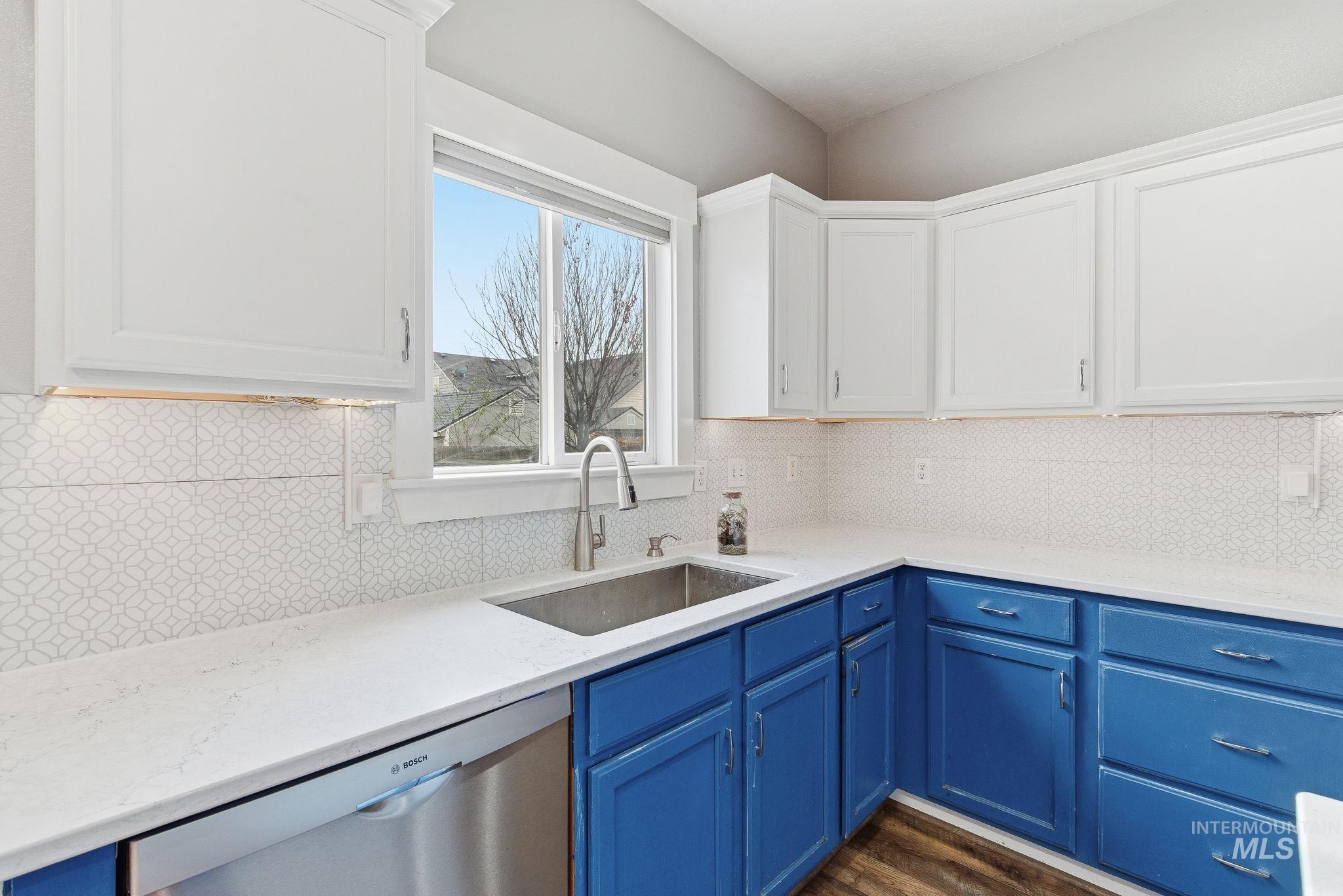 Kitchen featuring blue cabinets, dishwasher, white cabinets, and light stone countertops