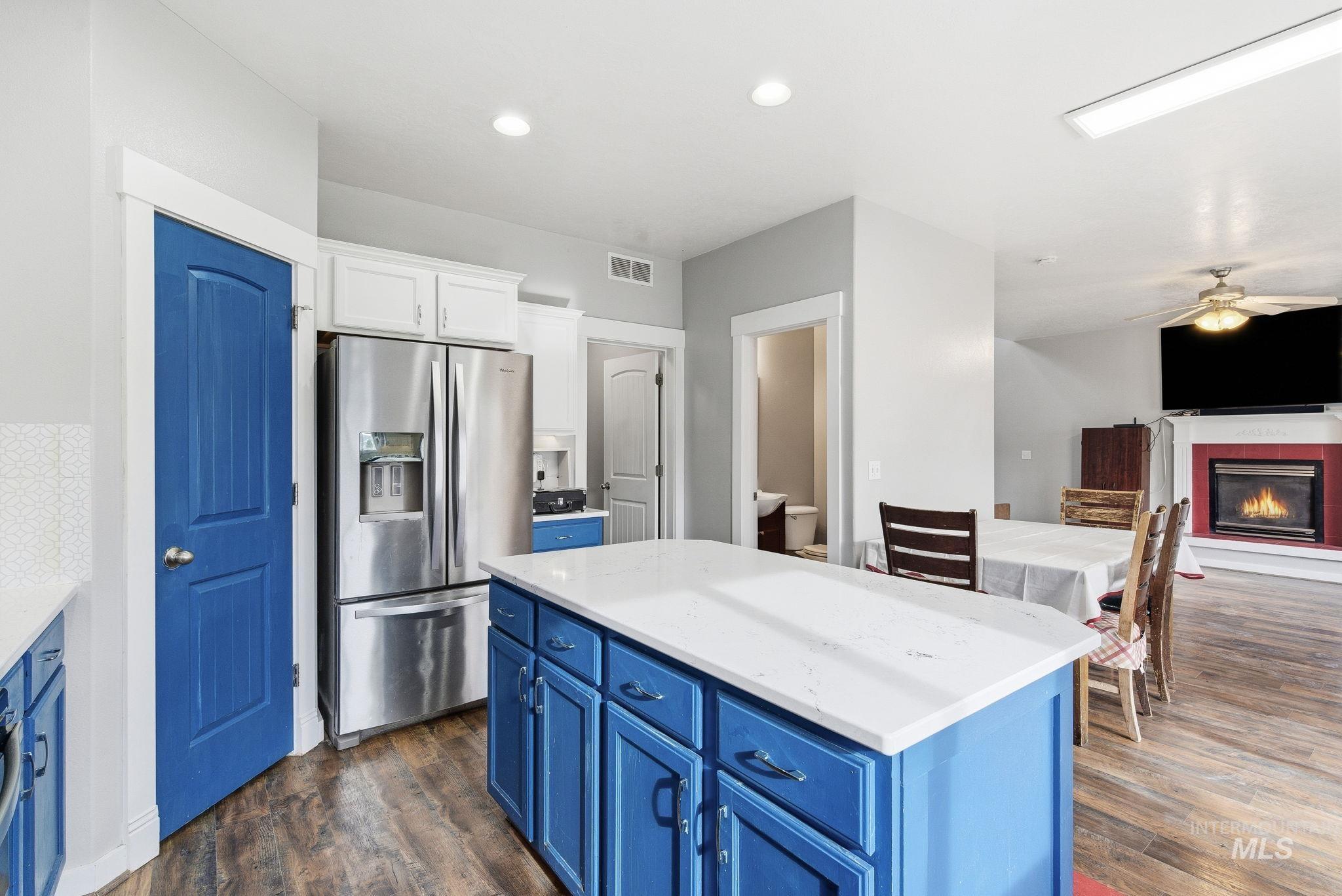 Kitchen with blue cabinetry, stainless steel fridge with ice dispenser, a center island, a glass covered fireplace, and white cabinets