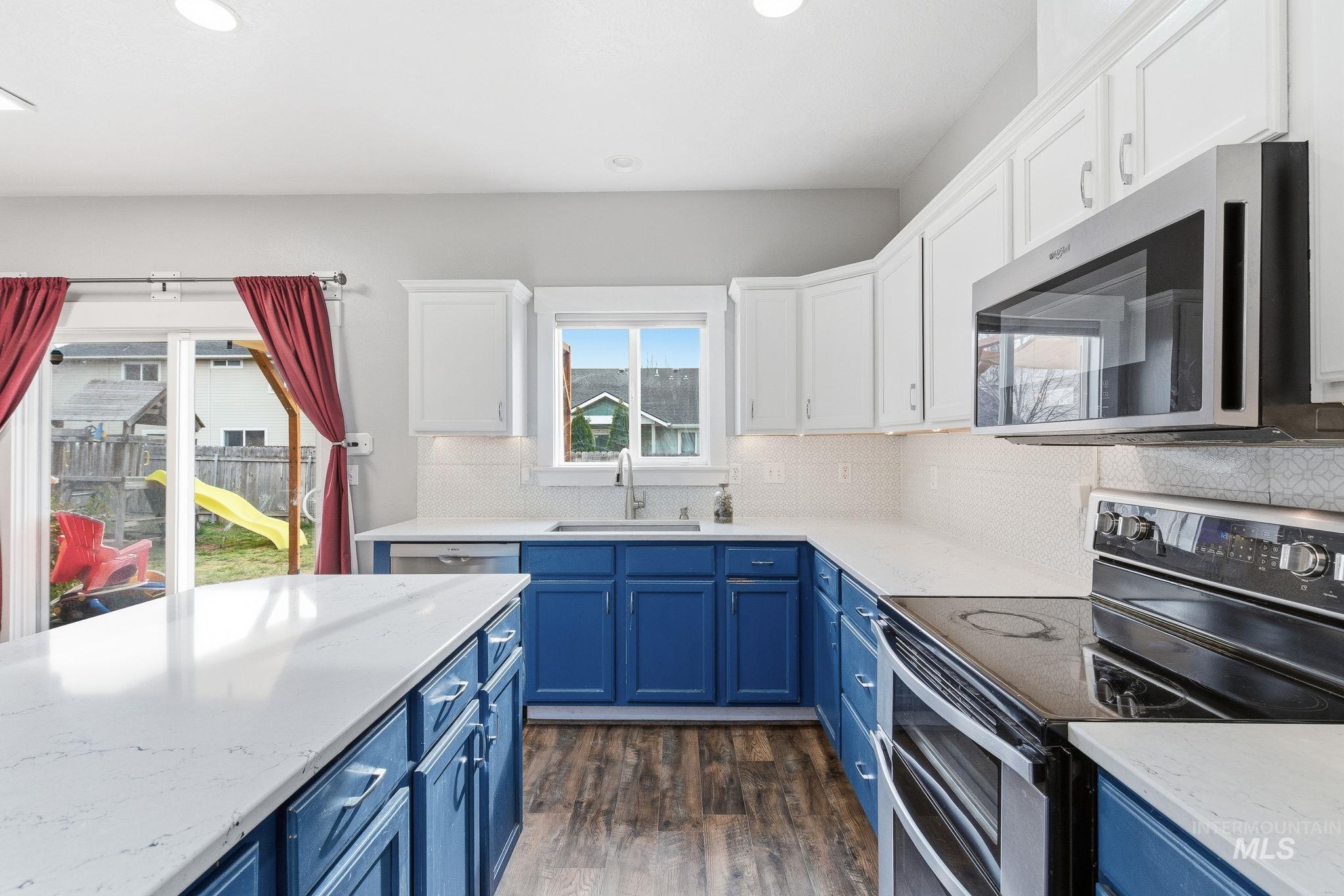 Kitchen featuring blue cabinetry, appliances with stainless steel finishes, light stone counters, white cabinetry, and recessed lighting