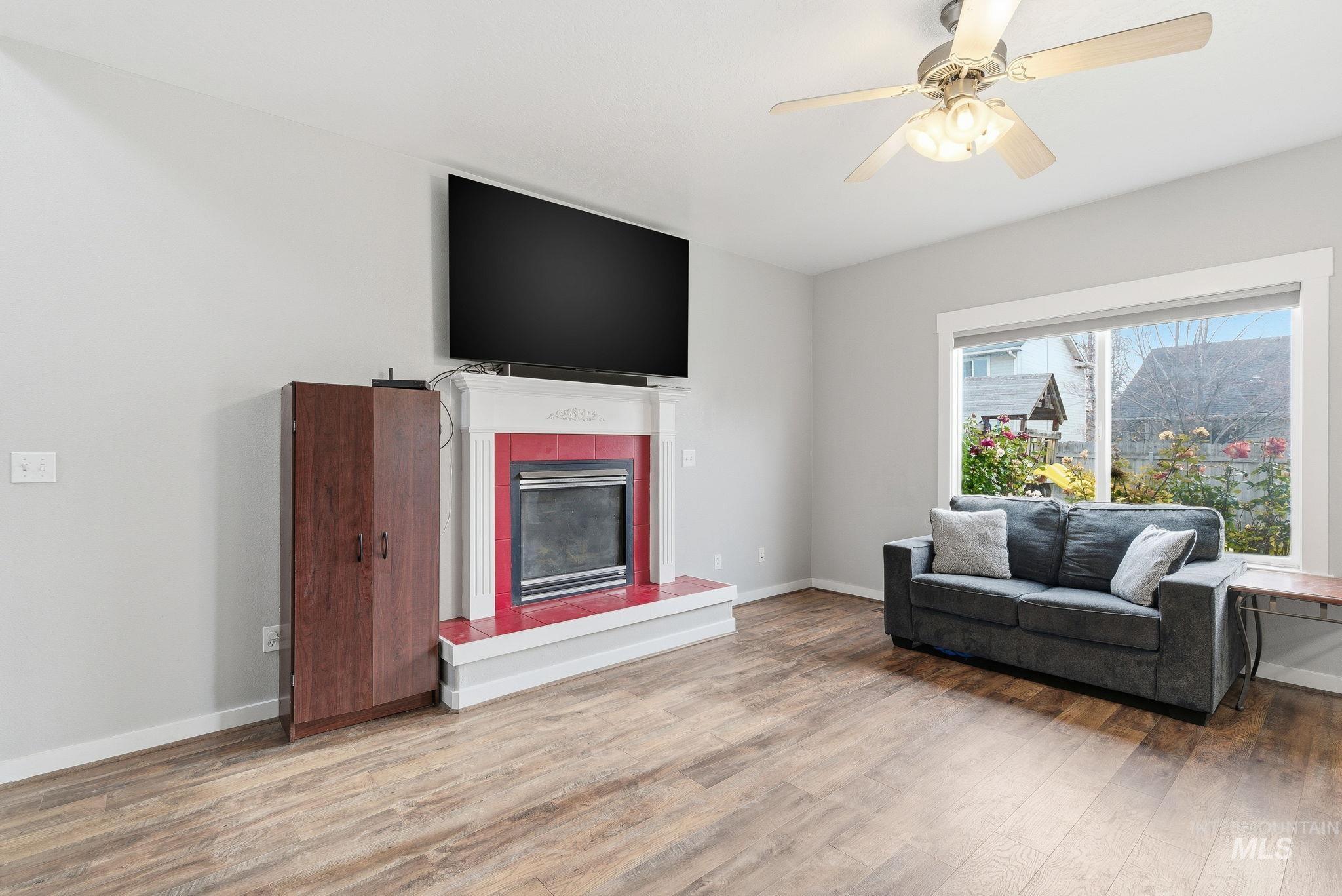 Living room with a fireplace, wood finished floors, and a ceiling fan