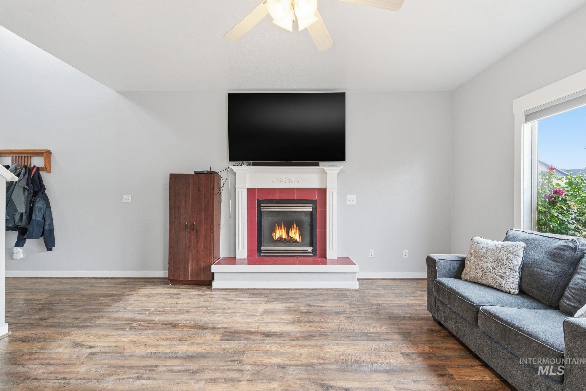 Living room featuring a tiled fireplace, wood finished floors, and a ceiling fan
