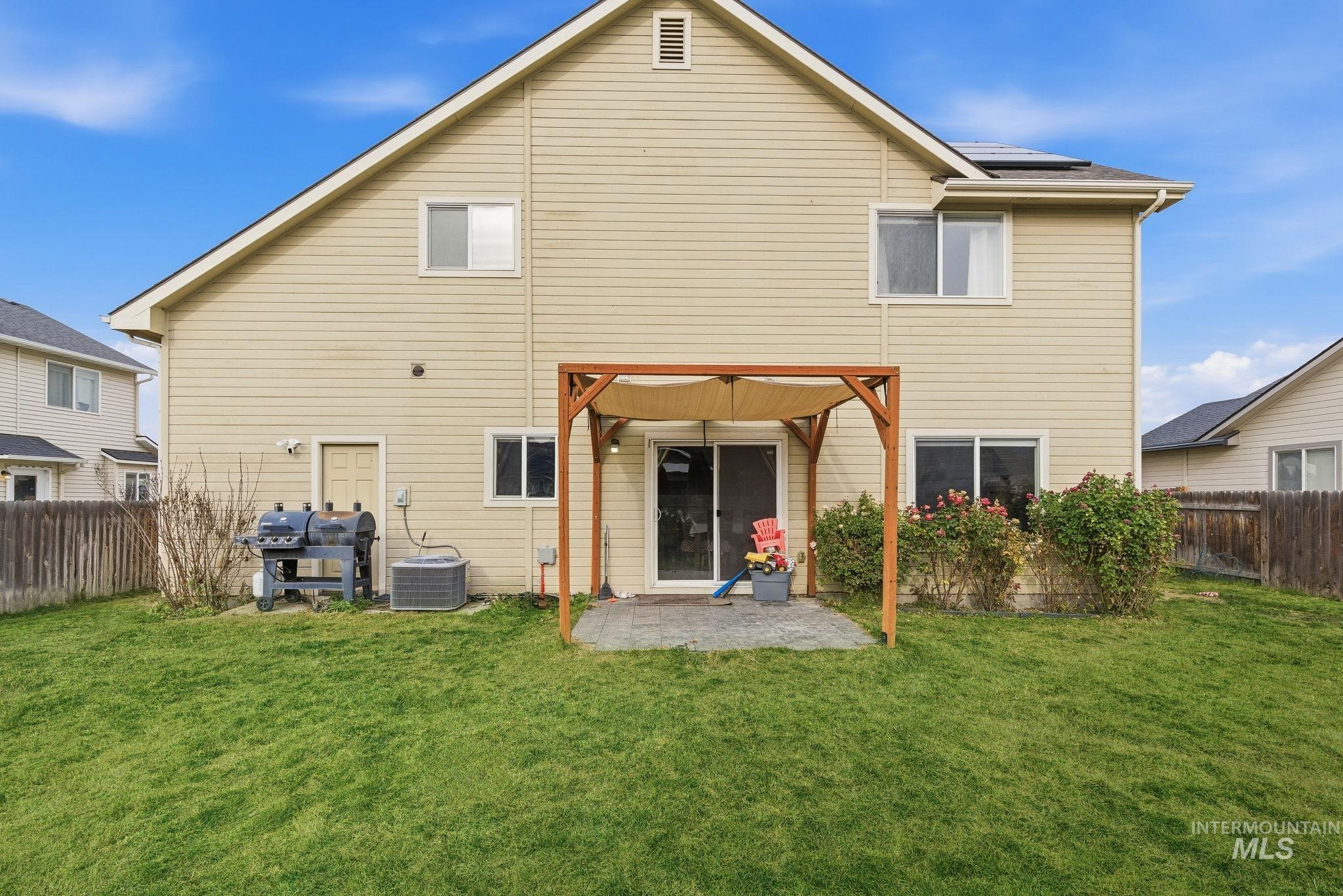 Back of property with a fenced backyard, a patio, and roof mounted solar panels
