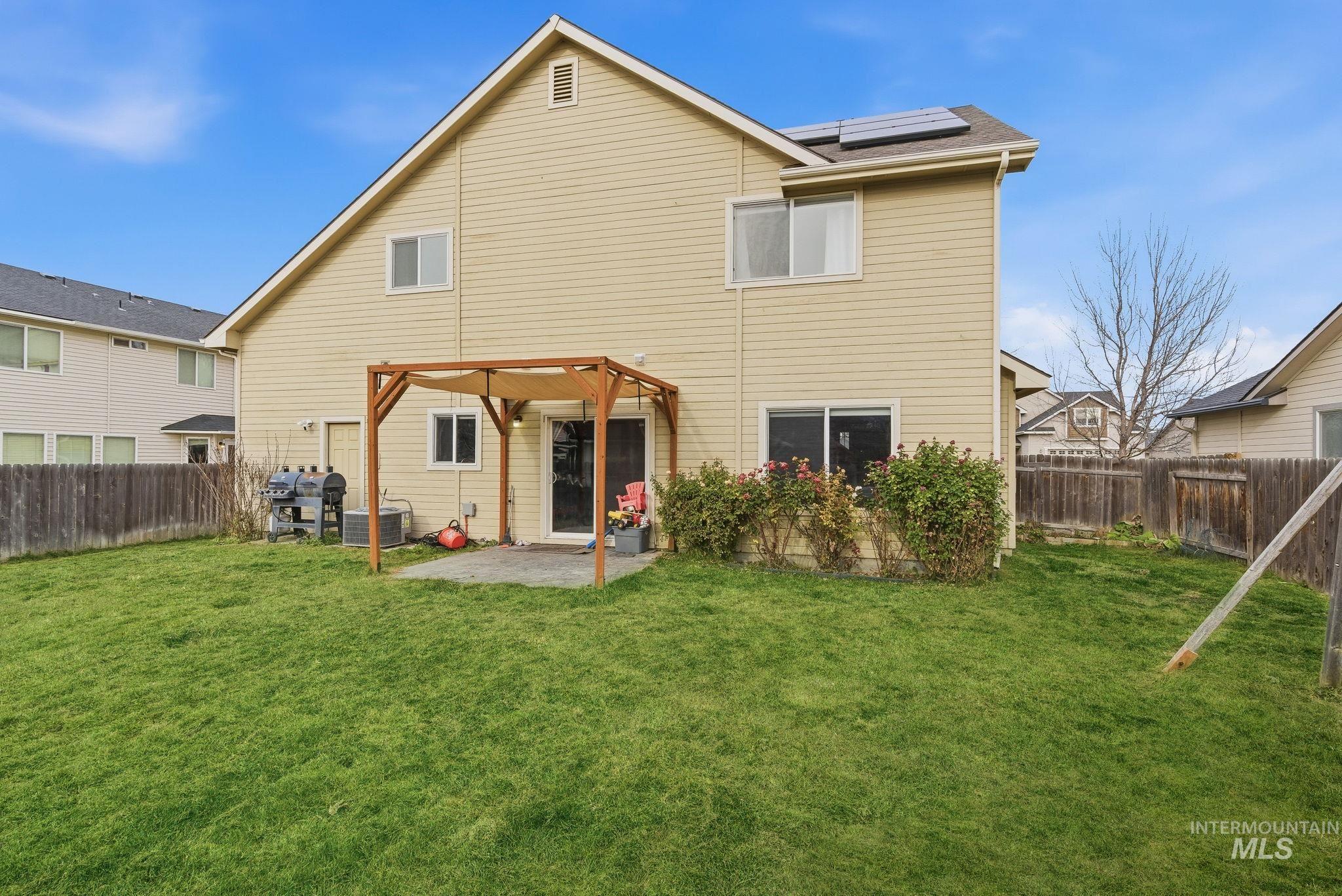 Rear view of house with a patio area, a fenced backyard, and roof mounted solar panels
