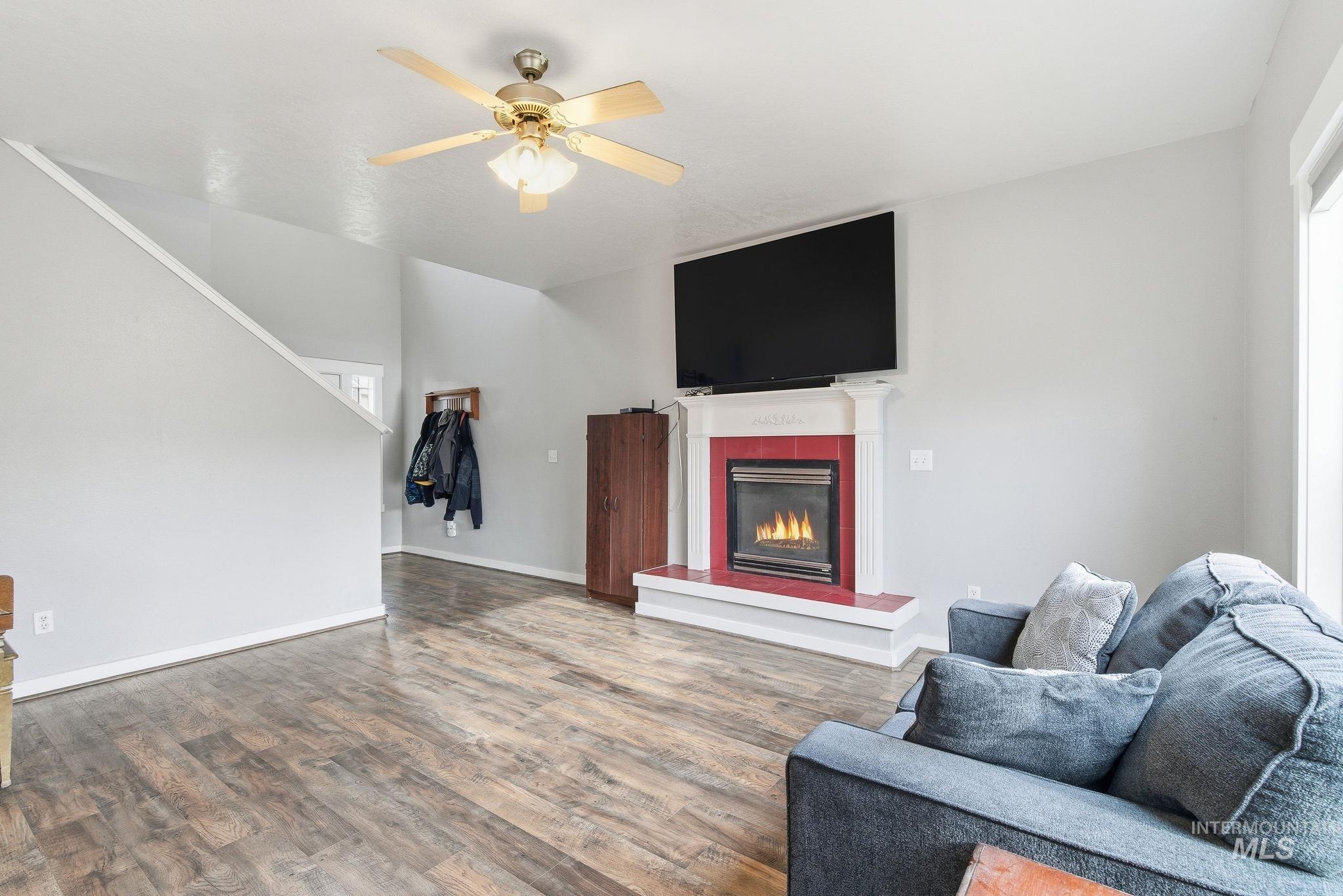 Living area with a tiled fireplace, wood finished floors, and ceiling fan