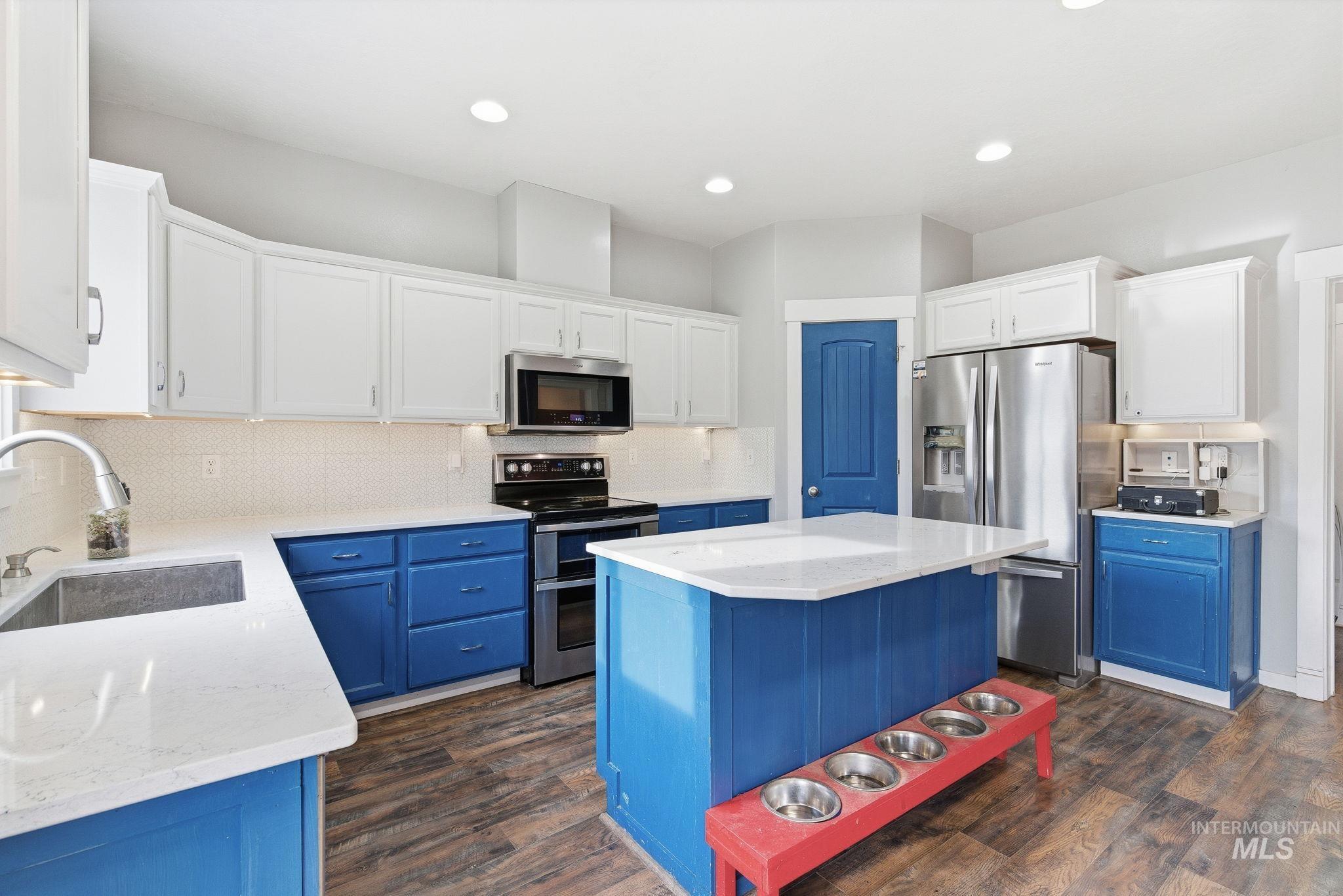 Kitchen with blue cabinets, appliances with stainless steel finishes, a center island, dark wood-style floors, and recessed lighting