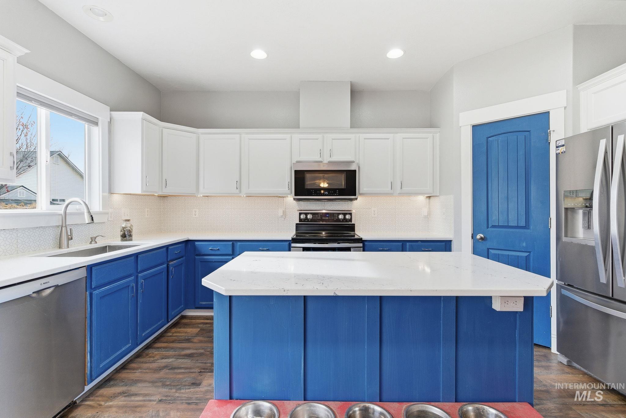 Kitchen with blue cabinetry, appliances with stainless steel finishes, a kitchen island, light stone counters, and white cabinetry
