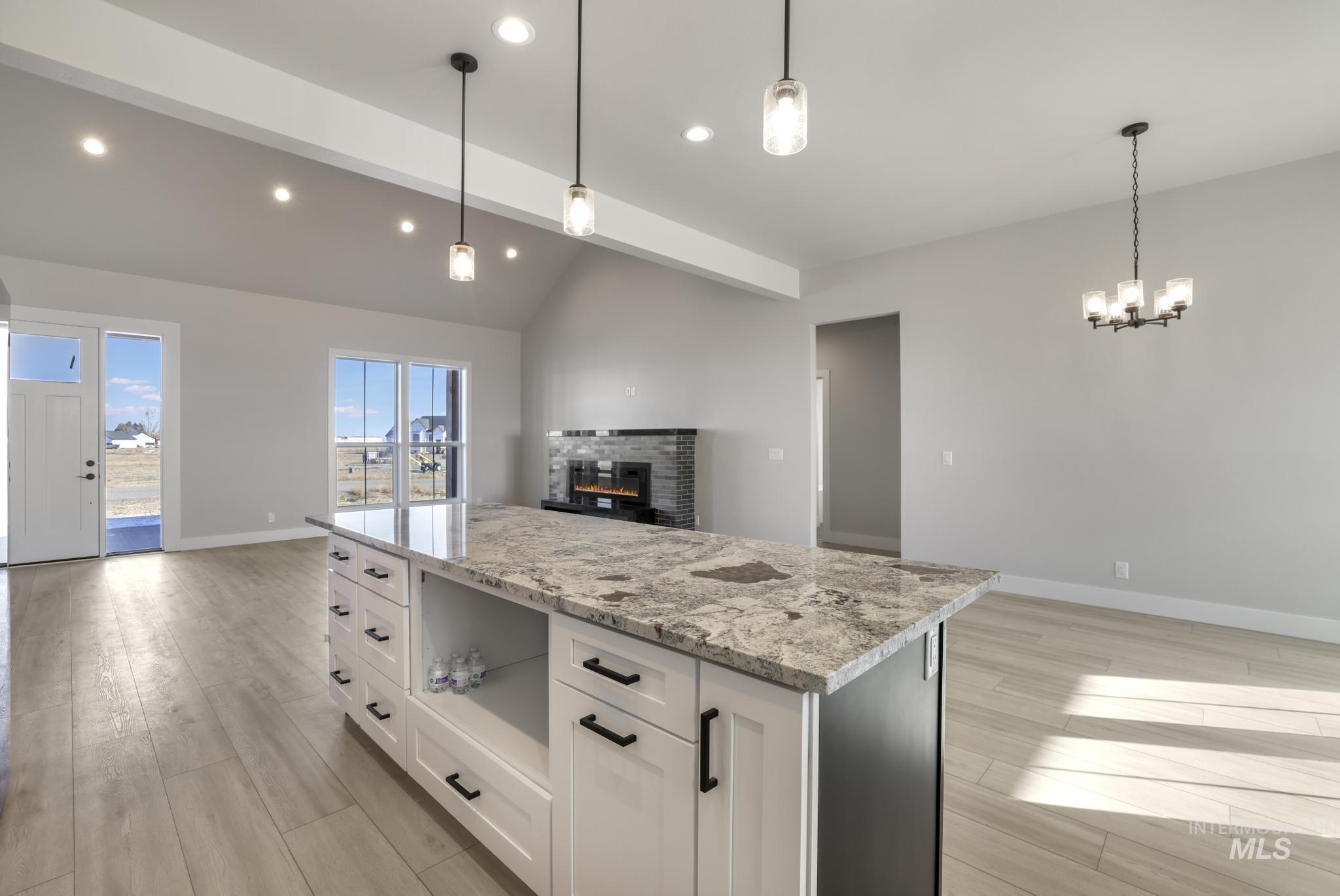 Kitchen featuring open floor plan, white cabinets, light stone countertops, a center island, and light wood-style floors