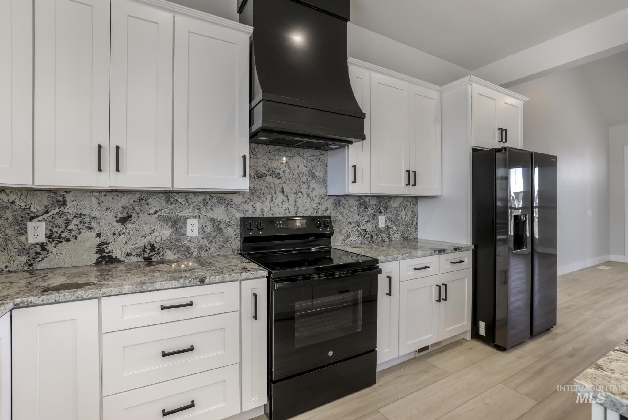 Kitchen with black appliances, white cabinetry, and custom range hood