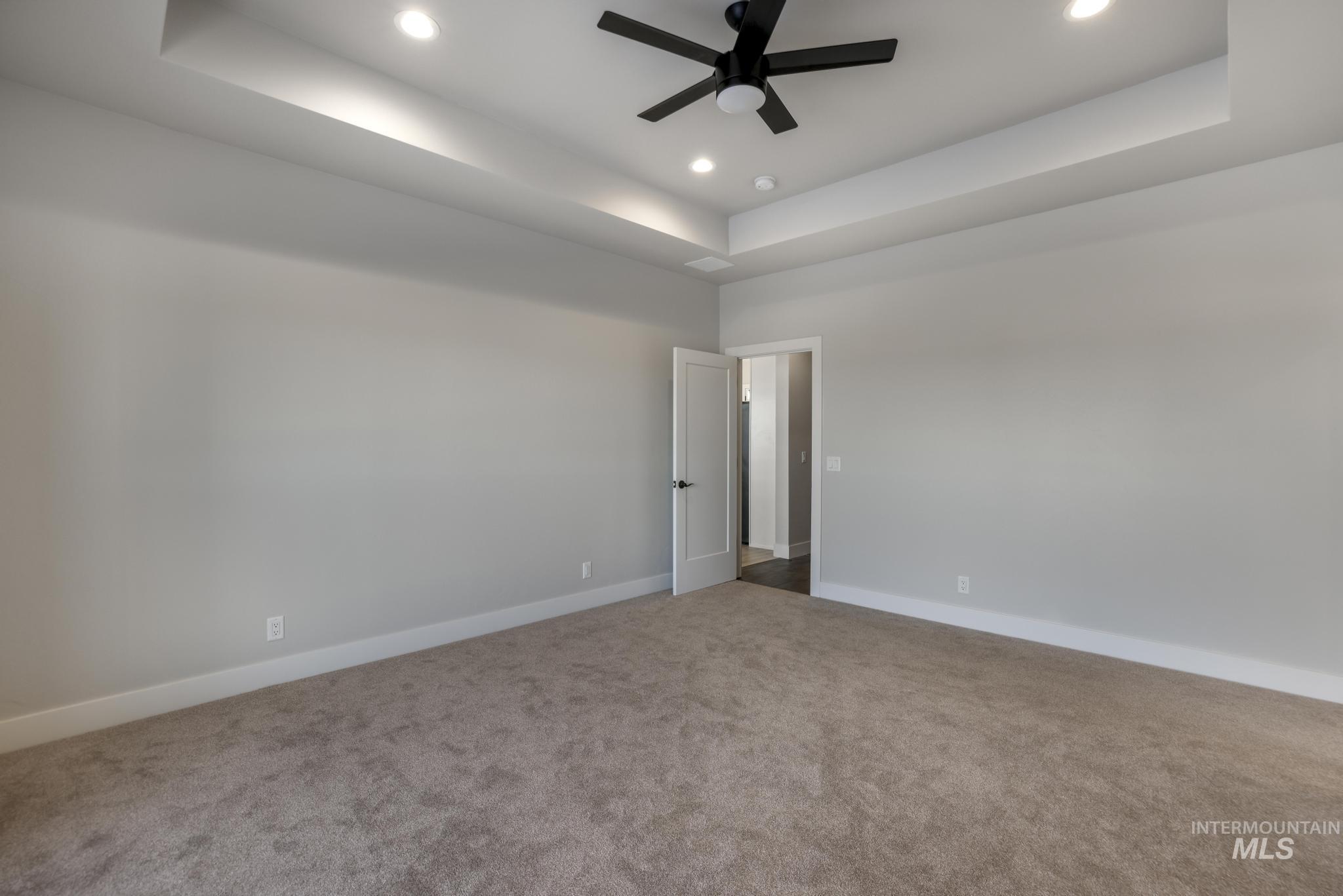 Carpeted empty room with a tray ceiling, recessed lighting, and a ceiling fan