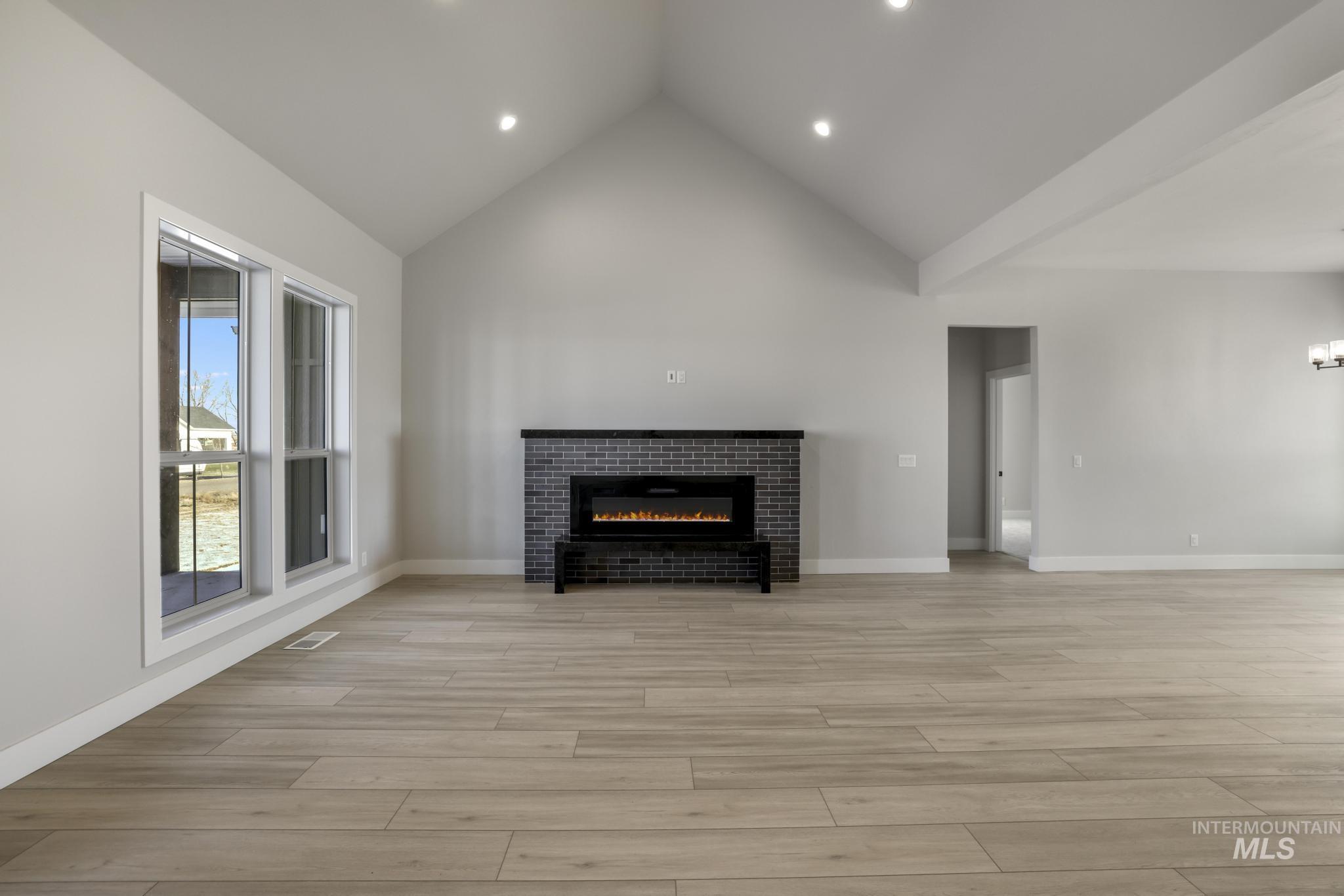 Unfurnished living room featuring a glass covered fireplace, light wood-style floors, high vaulted ceiling, and recessed lighting
