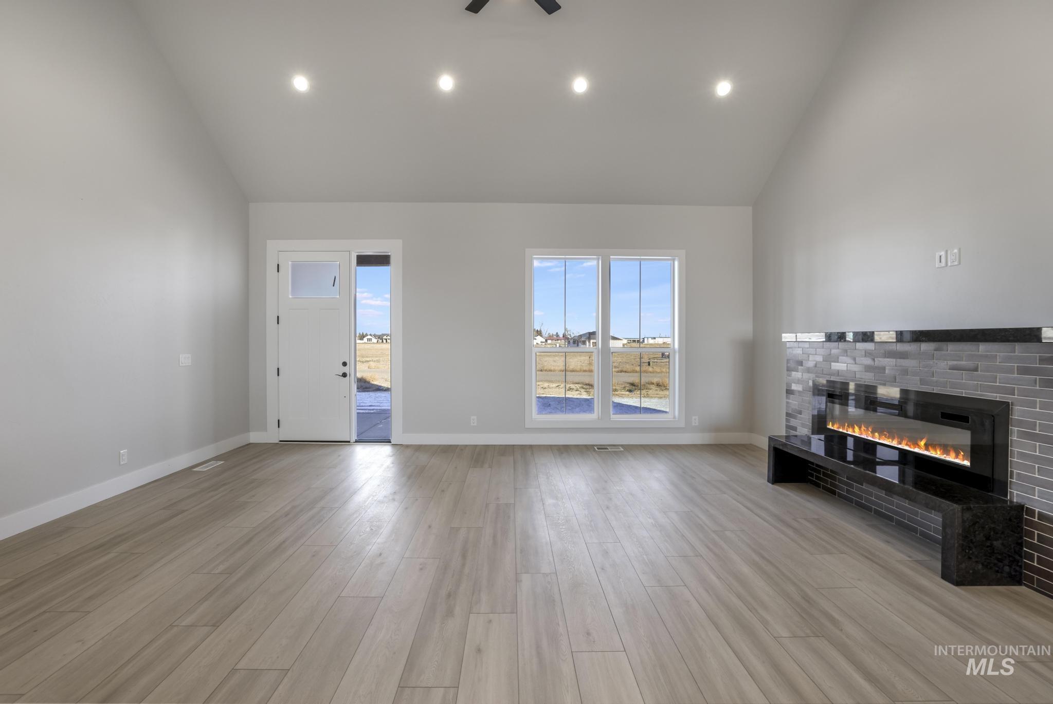 Unfurnished living room featuring high vaulted ceiling, light wood-style flooring, recessed lighting, and a brick fireplace