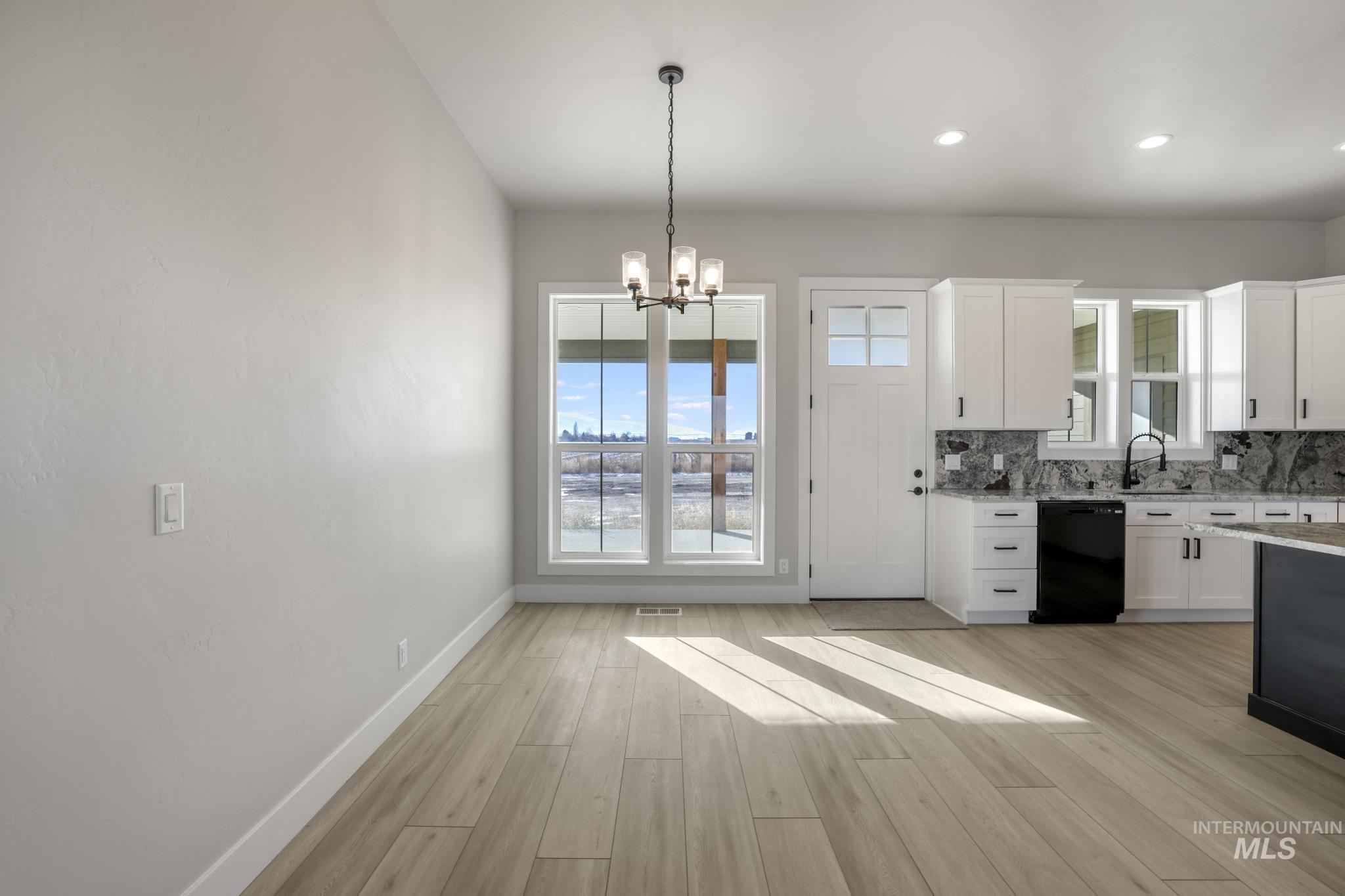 Kitchen featuring decorative light fixtures, white cabinetry, light stone countertops, a chandelier, and plenty of natural light