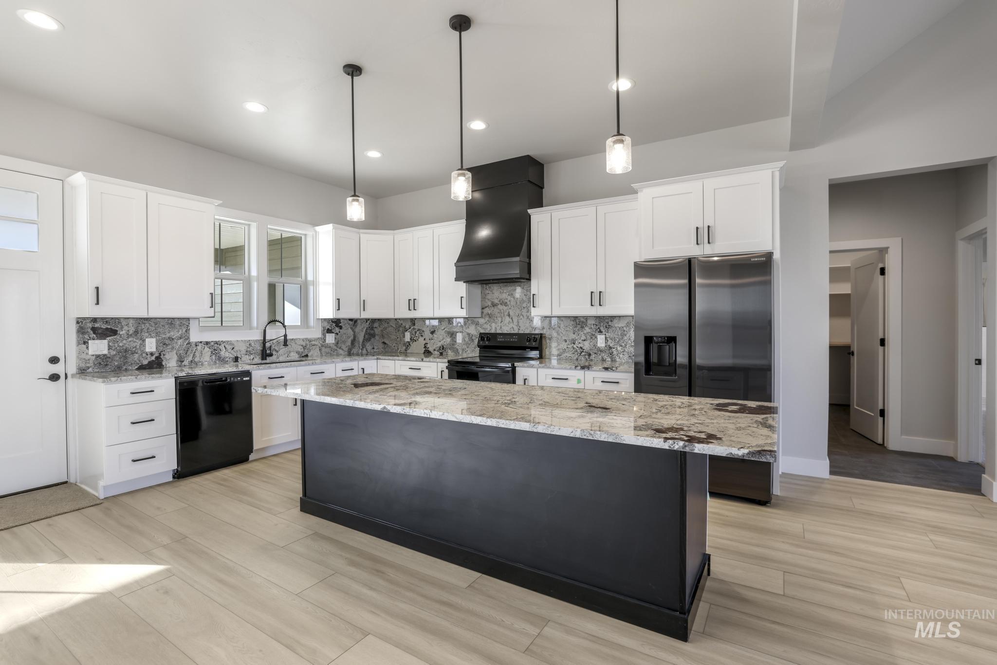 Kitchen with a center island, white cabinets, premium range hood, hanging light fixtures, and light stone counters