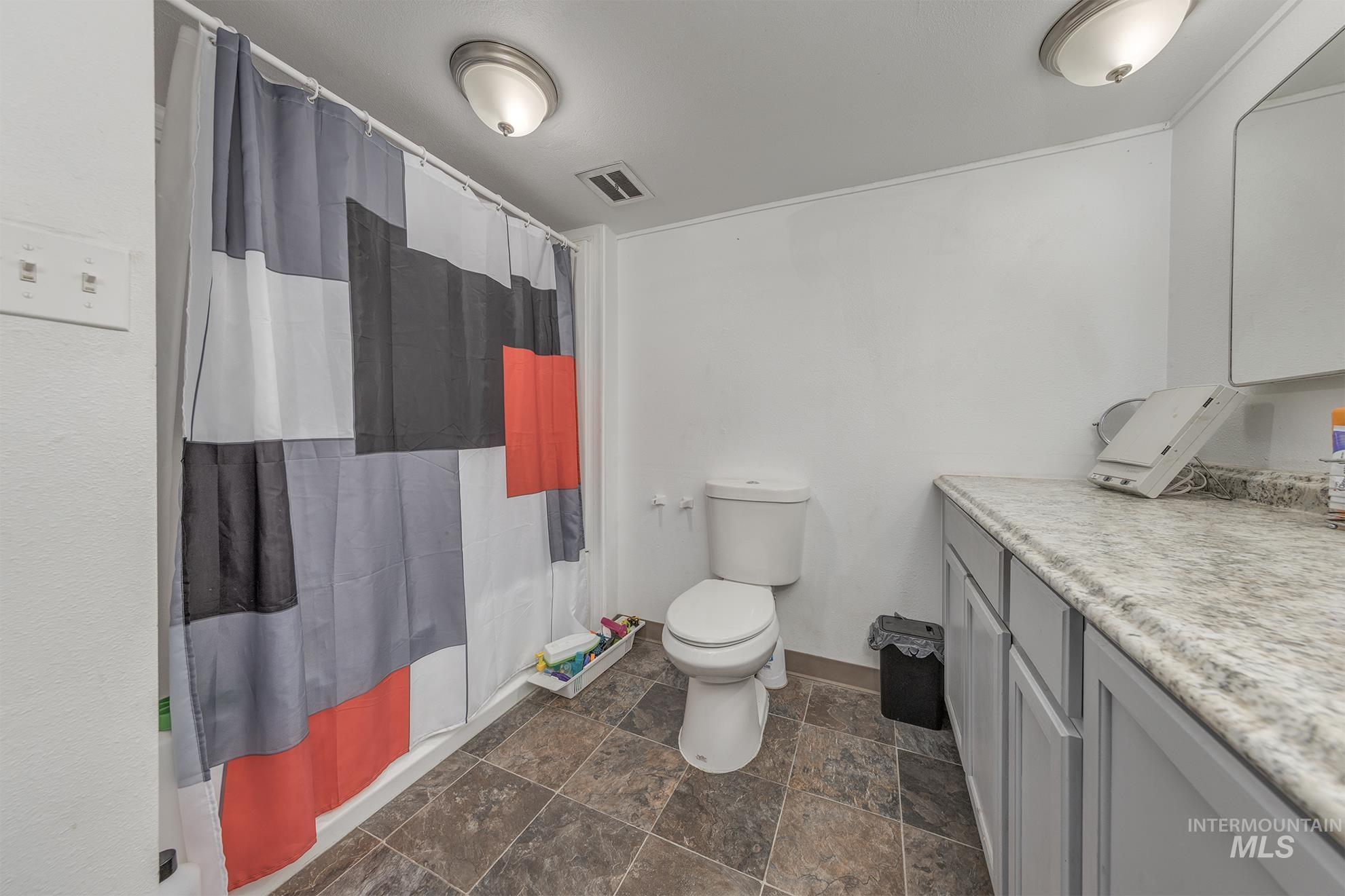 Bathroom with curtained shower, stone finish floors, and vanity