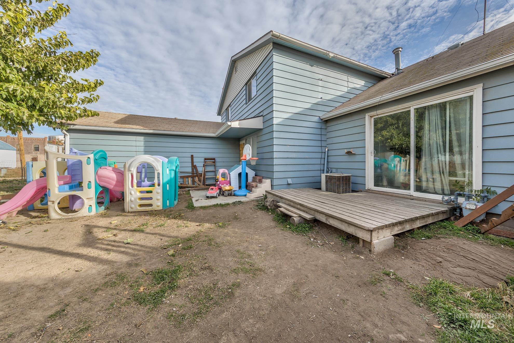 Back of property featuring a wooden deck, a shingled roof, and a playground