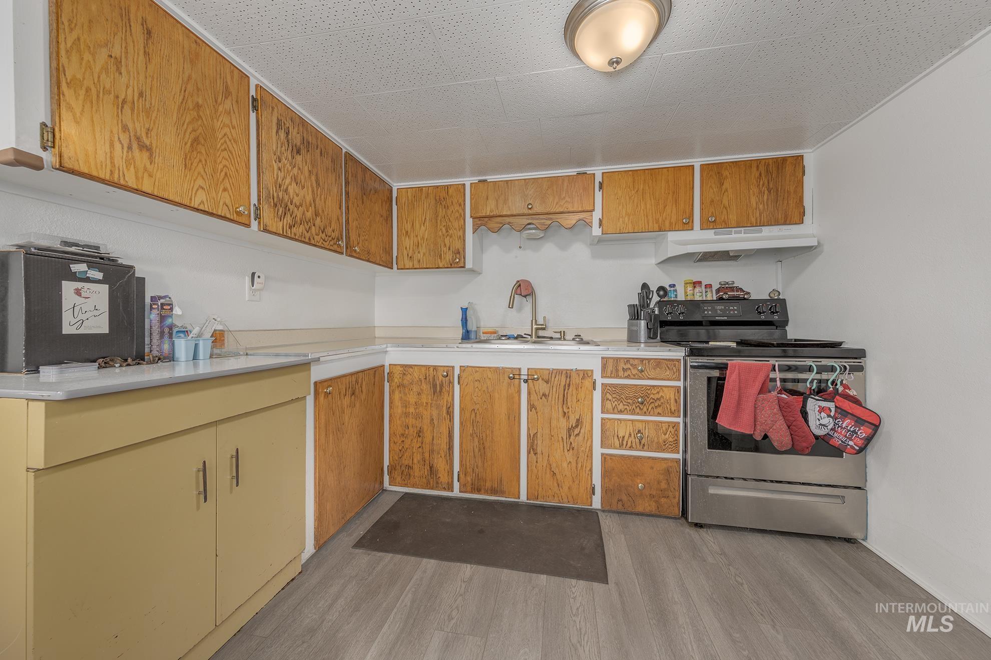 Kitchen featuring electric range, light countertops, light wood-type flooring, brown cabinetry, and under cabinet range hood