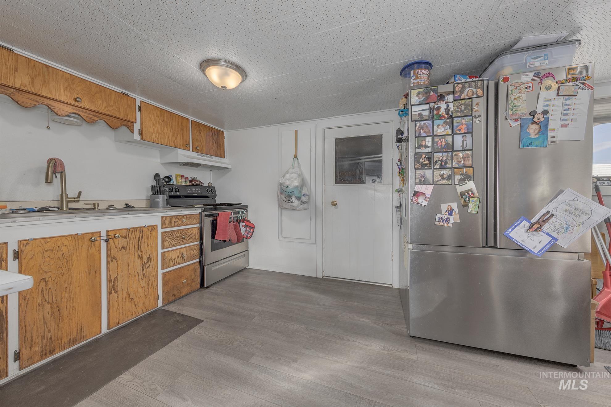 Kitchen featuring brown cabinets, stainless steel appliances, light countertops, light wood-style floors, and under cabinet range hood