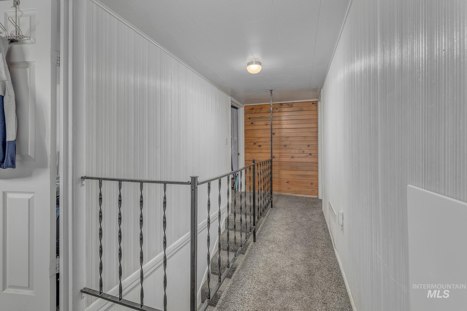 Hallway featuring carpet, wood walls, and an upstairs landing